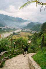 A person descends a stone path with arms raised, overlooking a misty valley, river, village, and...