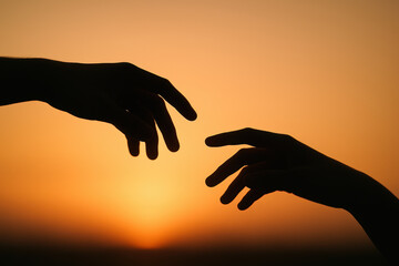 Two hands reaching out against a sunset background, silhouette of connection and hope