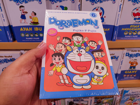 South Kalimantan, Indonesia - 06 09 2025 : Doraemon manga held by hand with additional comic books in background, ideal for youth, animation culture, or family-friendly editorial use