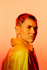 Obraz premium young woman with colorful shaved hair and intense expression wearing yellow jacket against orange background, vibrant style and bold fashion statement