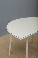 Minimalist wooden table with light finish and slim legs, placed in a simple interior with gray wall and wooden floor. Modern furniture design for dining, workspace, or home decor.