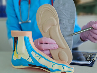 Medical demonstrating foot anatomy model alongside orthotic insole during patient consultation