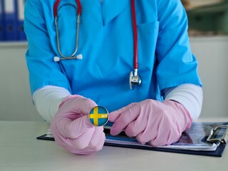 Nurse wearing gloves holds a medical badge representing Sweden in a healthcare