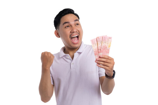 Excited young man celebrating with clenched fist while holding Indonesian rupiah money in hand isolated on transparent background