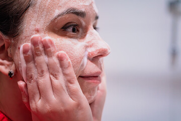 Naklejka premium A woman is applying a cleansing product to her face while looking in the mirror She is focused on addressing her problematic facial skin and demonstrates her skin care regimen