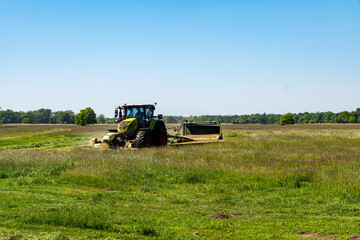 Modern green tractor mowing grass on open farmland