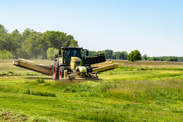 Tractor with wide mower cutting grass on green field