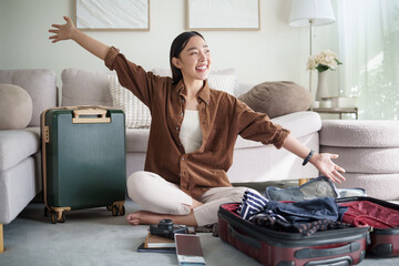 Cheerful young woman raising arms in excitement while packing her suitcase for an upcoming trip.