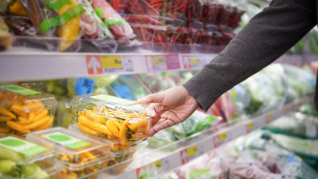 Hand picking fresh packaged yellow peppers from the vegetable shelf in modern supermarket