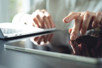Closeup, business woman using digital tablet, finger touching on screen, working with laptop computer on office desk. Graphic designer using graphic tablet designing creative project