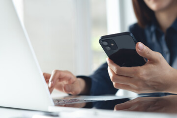 Young asian business woman using smartphone and working on laptop computer with digital tablet on office table. Businesswoman surfing the internet, closeup