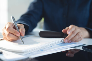 Close up, business woman writing in notebook while sitting at working place with laptop computer with financial report on office table. Businesswoman doing finance and making notes on notepad