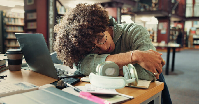Tired, man and student sleeping in library with burnout for studying with university test. Fatigue, education and person with afternoon nap for resting at desk laptop at college campus for exhaustion - Powered by Adobe