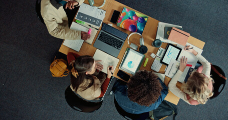 Technology, books and group of students studying in library for university test, project or exam. Top view, notes and friends preparing for college assignment together with scholarship at campus.