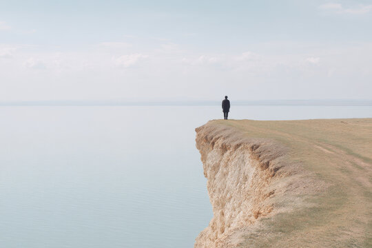 minimalist scene featuring solitary figure standing on coastal cliff in kazakhstan under overcast sky