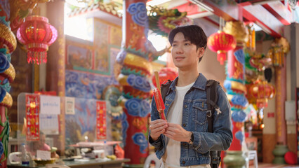 Young male traveler holding incense sticks while making a wish inside a Chinese temple.
