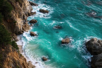Turquoise ocean waves crash against a rocky, tree-lined coastline, viewed from an elevated perspective