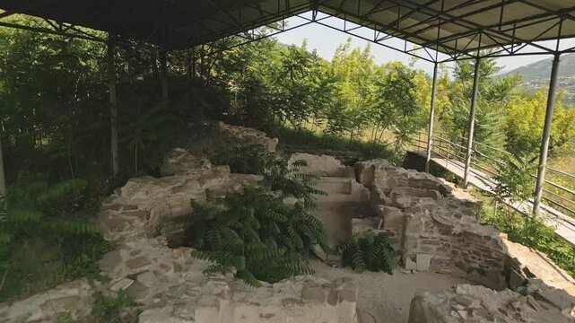 Walking point of view through Preserved remains of the ancient royal bath structure at Armaziskhevi site, surrounded by greenery under protective roof in Mtskheta region, Georgia