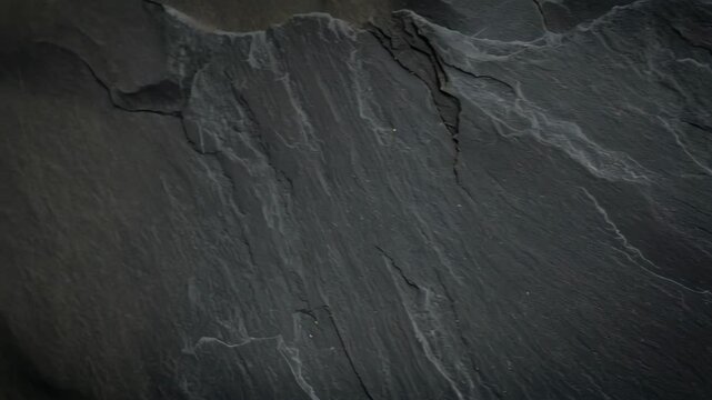 Detailed close-up of dark gray slate rock surface with intricate patterns and subtle texture variations for background applications