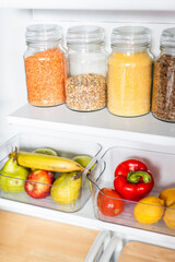 organized tidy decluttered pantry with matching clear jars of healthy ingredients like grains, legumes, spices, fruit and vegetables