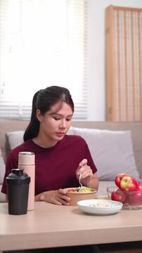 Asian woman sitting and eating cereal and yogurt, part of a healthy post-workout meal
