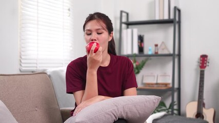 Young woman biting an apple while relaxing on sofa with pillow - Powered by Adobe