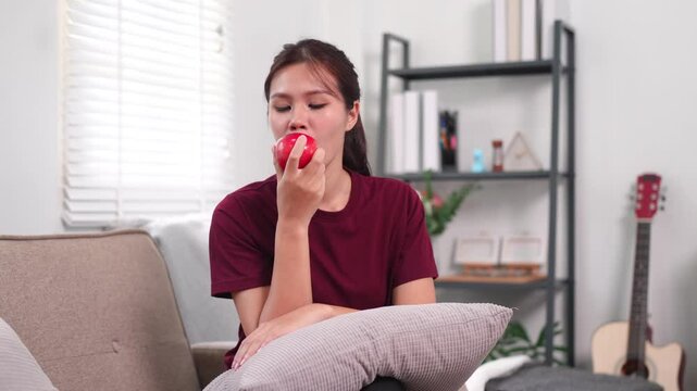 Young woman biting an apple while relaxing on sofa with pillow