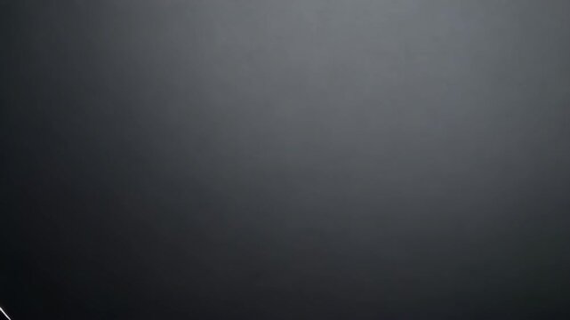 High angle video of a sharp chef's knife laying on a dark gray surface. Steel blade features distinct textured patterns for food preparation.