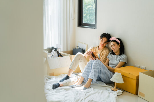Young couple sitting on bed in new house surrounded by moving boxes, enjoying quiet moment together with book, feeling happy and relaxed in their new home
