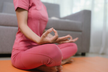 Young Asian woman meditating on a yoga mat with headphones in to promote relaxation and wellbeing at home.