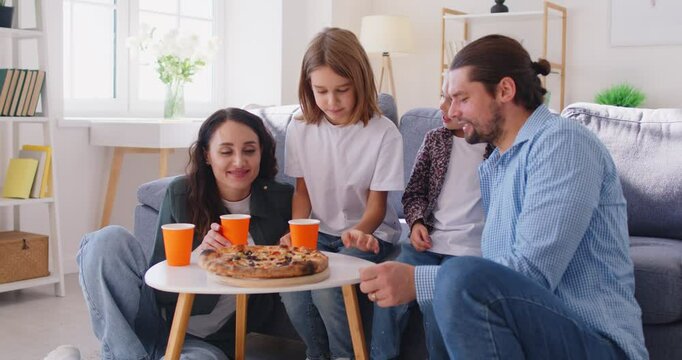 Positive parents with kids in family setting enjoy dinner at home, eating pizza together for lunch during leisure, creating joyful moments in a cozy environment with connection and warmth.