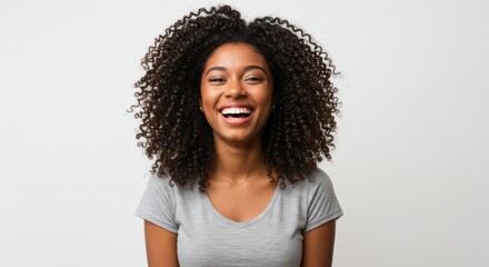 Portrait of a beautiful young African American woman with big curly hair smiling joyfully at the camera on a light background.