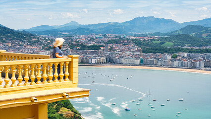Obraz premium Tourist woman leaning out of a balcony overlooking La Concha Bay in San Sebastian, Basque Country.