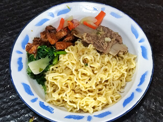 Guring beef noodle soup, equipped with delicious toppings, served on a traditional Indonesian iron plate.