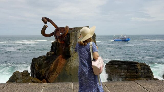Tourist woman with her back to her watching the waves break violently against the rocks on the shore,