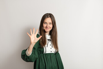 A woman with long hair wearing a green dress stands against a plain background. She smiles and...