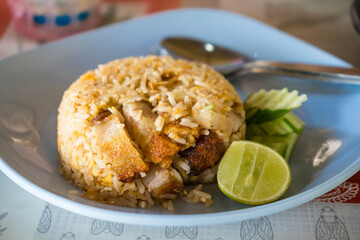 Delicious serving of Thai chicken fried rice with fresh lime and cucumber slices on a blue plate with a spoon.
