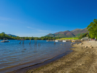Calm Derwentwater lakeside with a jetty, grassy park and mountains in the distance (Keswick, Lake District, England, United Kingdom)