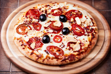 Pizza with salami and mozzarella cheese, jalapeno pepper and black olives. Wooden background. Soft focus. Close up.	