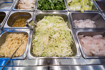 Buffet selection with shredded cabbage, fish slices, sauces, and fresh vegetables in stainless...