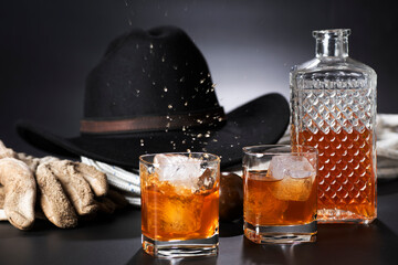 Whisky con ghiaccio su sfondo nero con cappello e guanti.