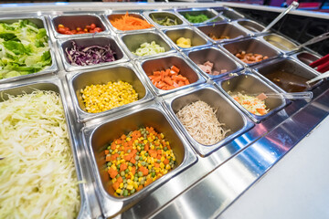A variety of fresh ingredients displayed in a salad bar with stainless steel containers and colorful vegetables.