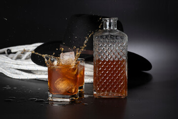 Whisky con cubetti di ghiaccio e cappello nero su sfondo nero