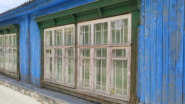 Large windows of an old wooden building. Double window frames with iron bars. Blue facade of house and green architraves