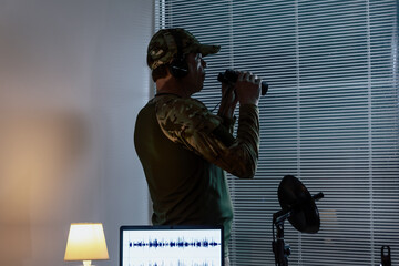 A man in military uniform with binoculars observing through the blinds. Modern concept of...