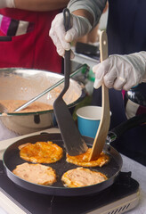 Gloved hands flip kimchi pancakes in a frying pan at a South Korea Embassy stall, with batter in a bowl nearby, during a cultural and food festival in Prague.
