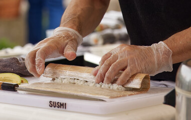 Close-up of chef using a bamboo mat while preparing fresh sushi rolls on a cutting board.