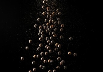 Scattering of whole black peppercorns suspended in air against a black studio backdrop image
