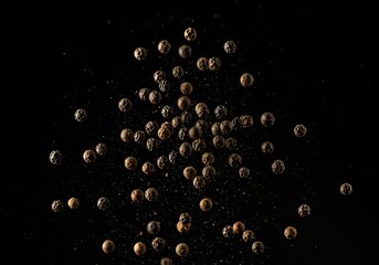 A scattering of dried black peppercorns against a stark black background in a studio shot style