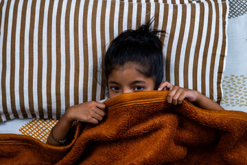 Child hiding under blanket in cozy bedroom setting
